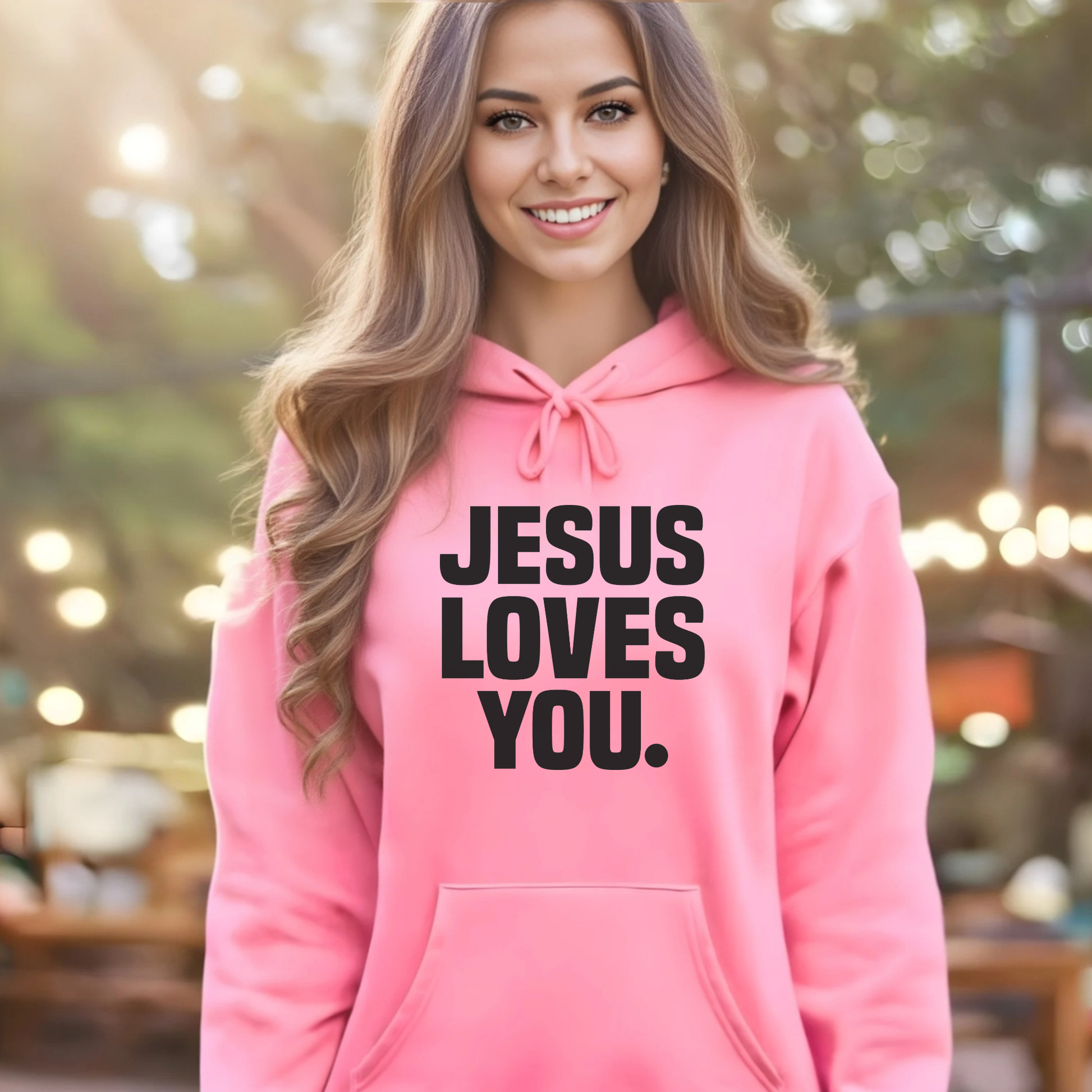 Woman wearing a pink hoodie with 'Jesus Loves You' text, standing outdoors.