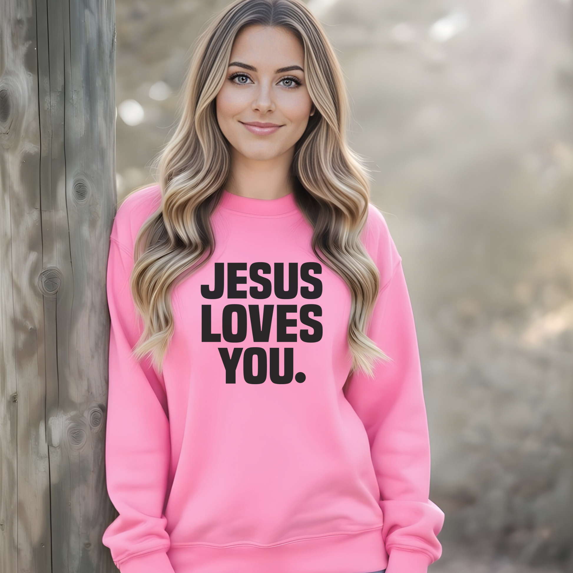 Woman wearing a pink sweatshirt with 'Jesus Loves You' text against a natural background
