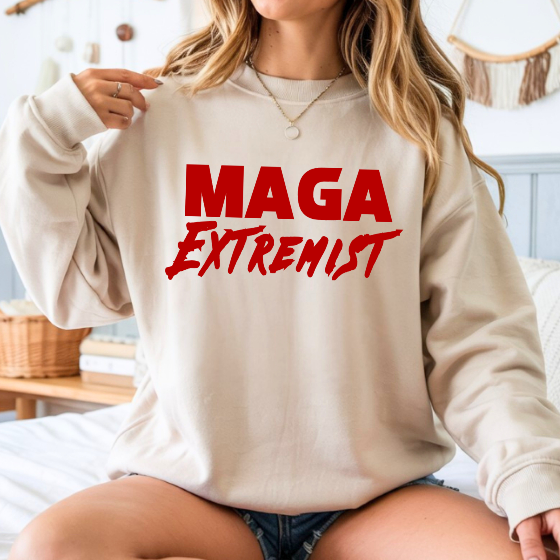 Person wearing a beige sweatshirt with 'MAGA Extremist' text in red.