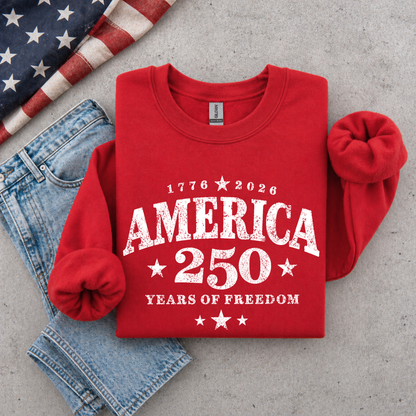 Red sweatshirt with 'America 250 Years of Freedom' text on a concrete surface with jeans and an American flag.