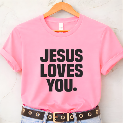 Pink t-shirt with 'Jesus Loves You' text on a hanger against a white background