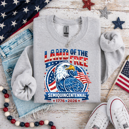 Gray America 250 sweatshirt with eagle design and text on a wooden surface with American flags and shoes.