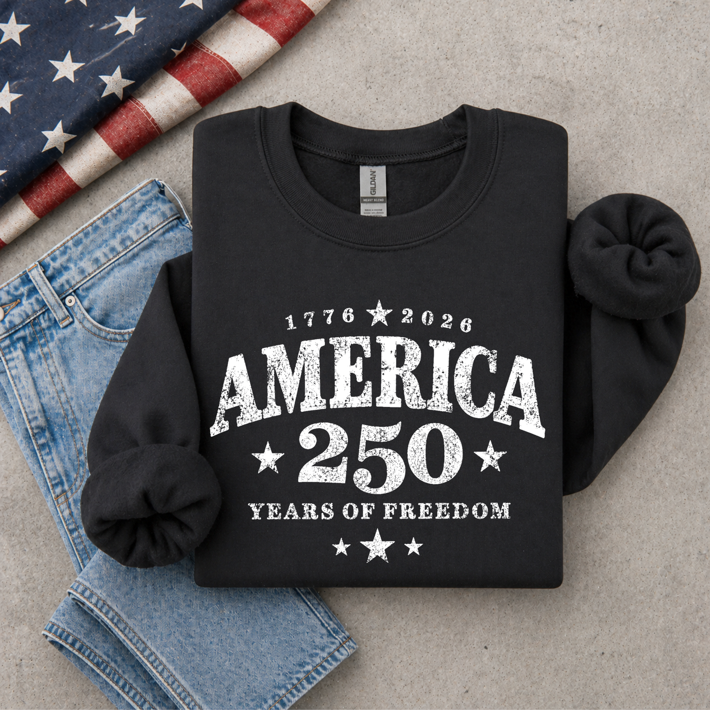 Black sweatshirt with 'America 250 Years of Freedom' text on a gray surface with denim and an American flag.