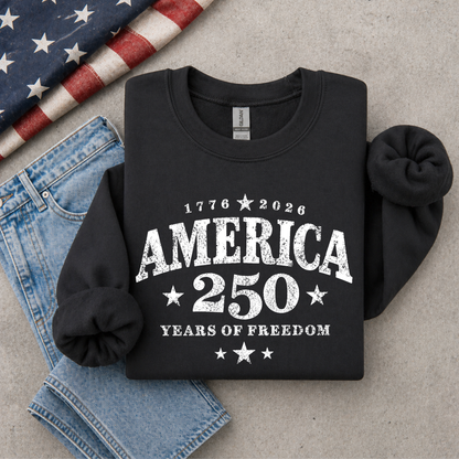 Black sweatshirt with 'America 250 Years of Freedom' text on a gray surface with denim and an American flag.