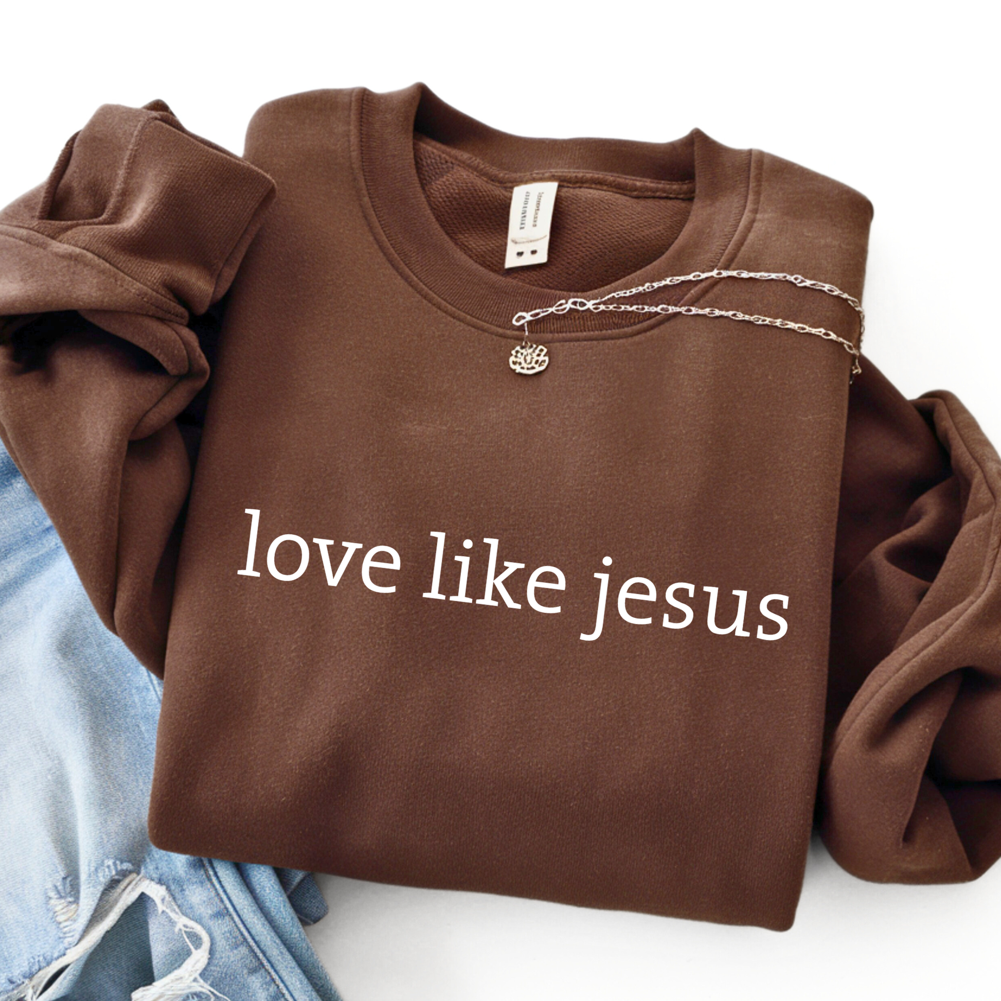 Flat lay navy blue sweatshirt with “love like jesus” white text design and silver necklace detail