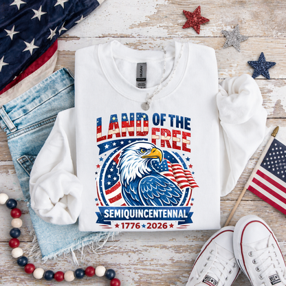 White sweatshirt with 'Land of the Free' design featuring an eagle and American flag, placed on a wooden surface with patriotic decor.