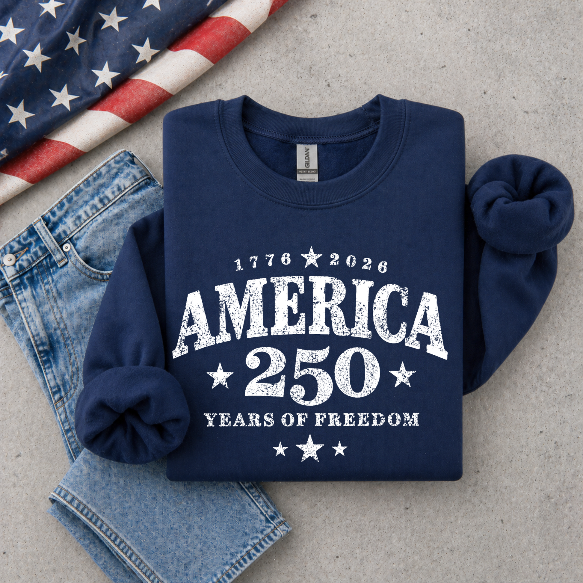 Navy blue sweatshirt with 'America 250 Years of Freedom' text, American flag, and jeans on a gray surface