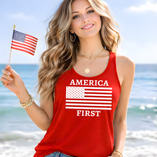 Woman wearing a red tank top with 'AMERICA FIRST' text and an American flag, holding a small American flag on a beach.