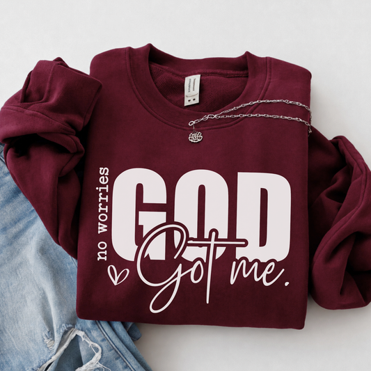 Maroon No Worries God Got Me crewneck sweatshirt flat lay with bold white lettering styled with denim.