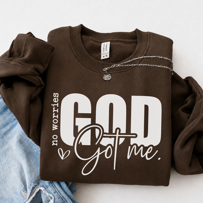 Brown No Worries God Got Me crewneck sweatshirt flat lay with bold white lettering, styled with denim.