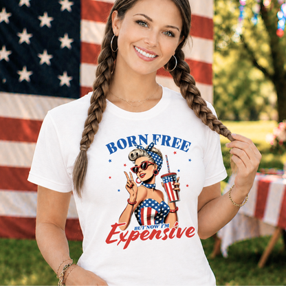 Woman wearing a 'Born Free But Now I'm Expensive' t-shirt with an American flag in the background.