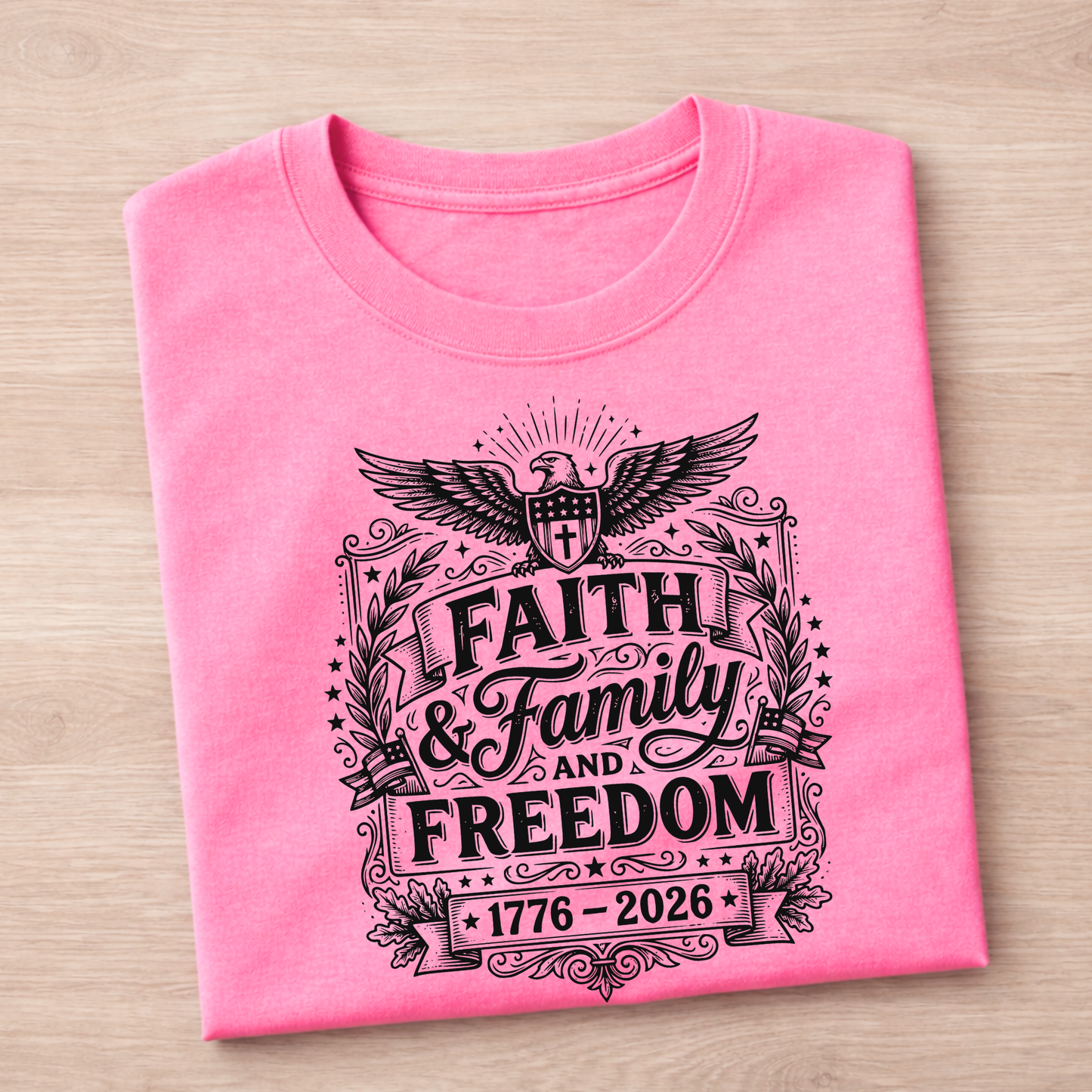 Folded pink Eagle 1776-2026 t-shirt with black graphic design on a wooden surface