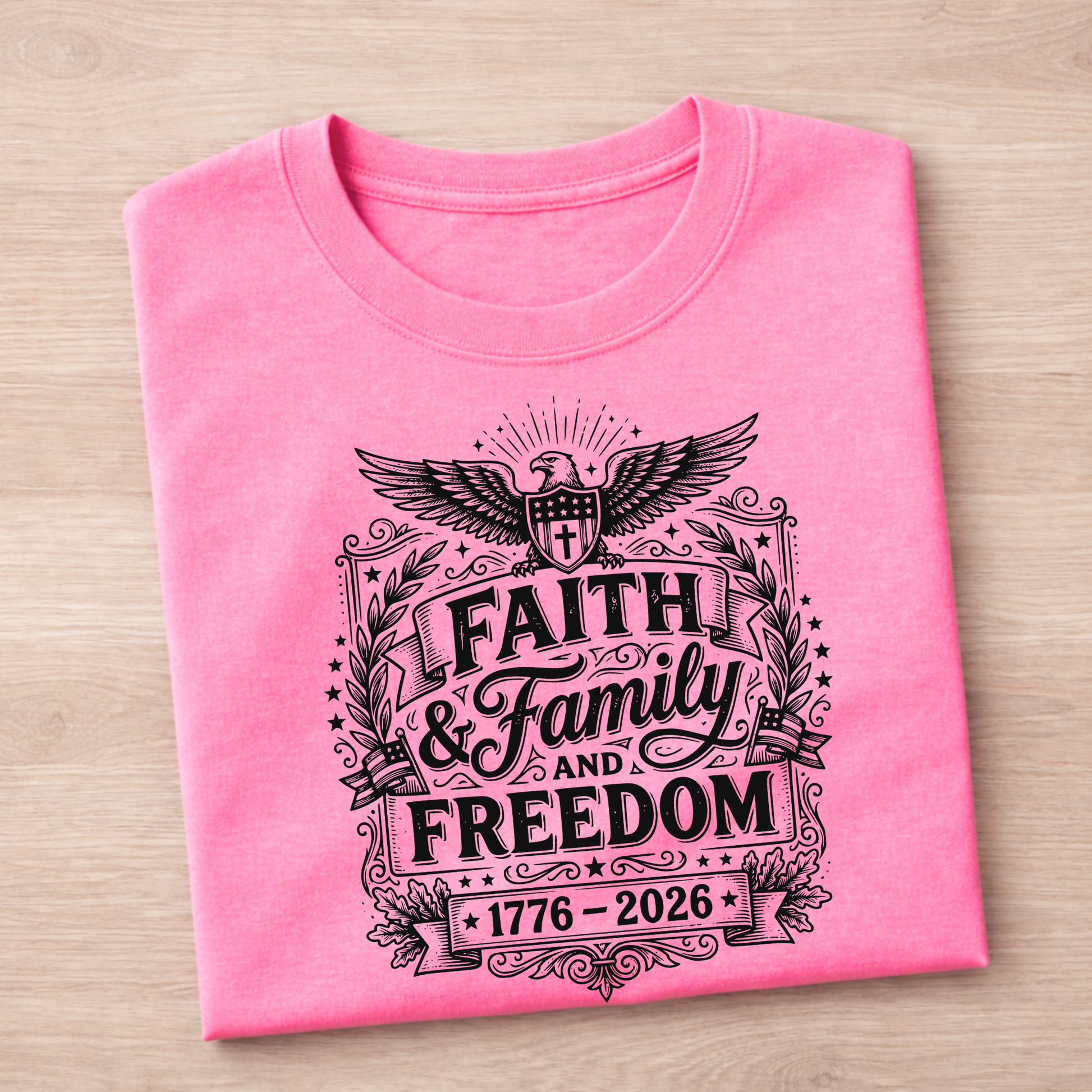 Folded pink Eagle 1776-2026 t-shirt with black graphic design on a wooden surface