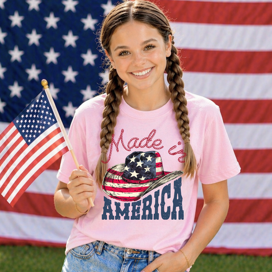 Girl holding an American flag and wearing a pink t-shirt with 'Made in America' text in front of an American flag background.
