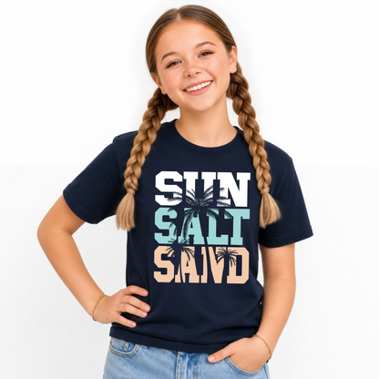 Smiling girl wearing a navy youth T-shirt with a stacked Sun Salt Sand graphic in white, aqua, and peach with black palm trees.