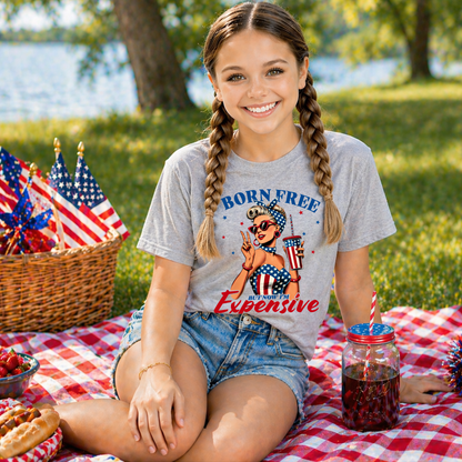Girl wearing a 'Born Free, Expensive' t-shirt at a picnic with American flags in the background.