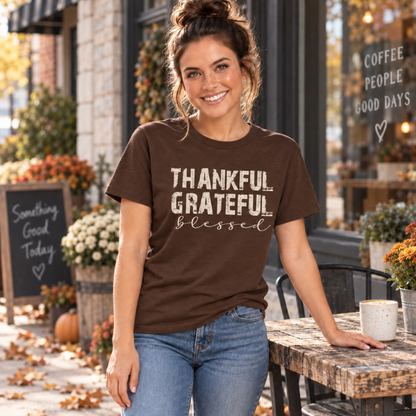Woman wearing a brown T-shirt with Thankful Grateful Blessed text beside an outdoor cafe table in fall.