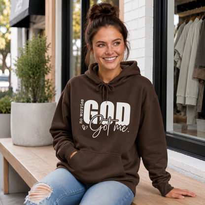 Woman wearing a brown No Worries God Got Me hoodie with bold white graphic lettering outside a boutique.