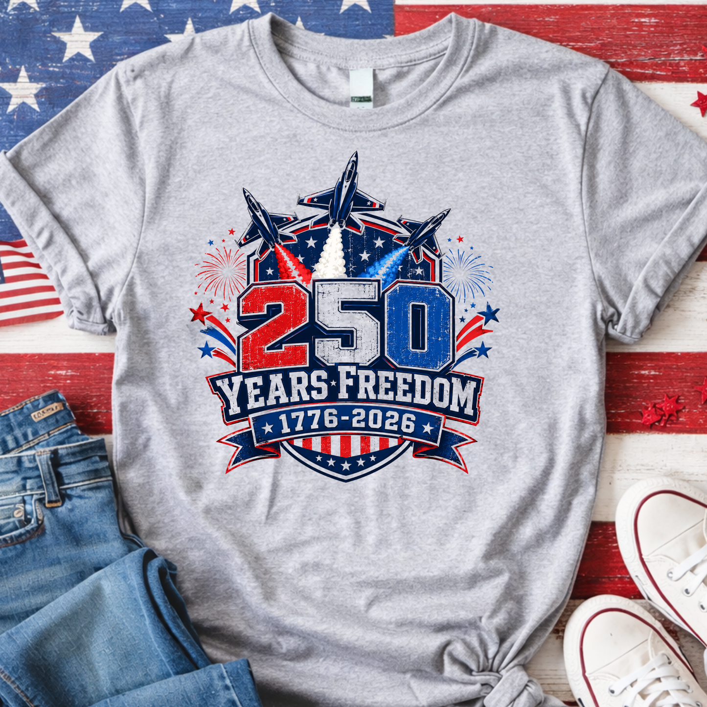 Gray t-shirt with '250 Years Freedom 1776-2026' design on a wooden surface with American flag and jeans.