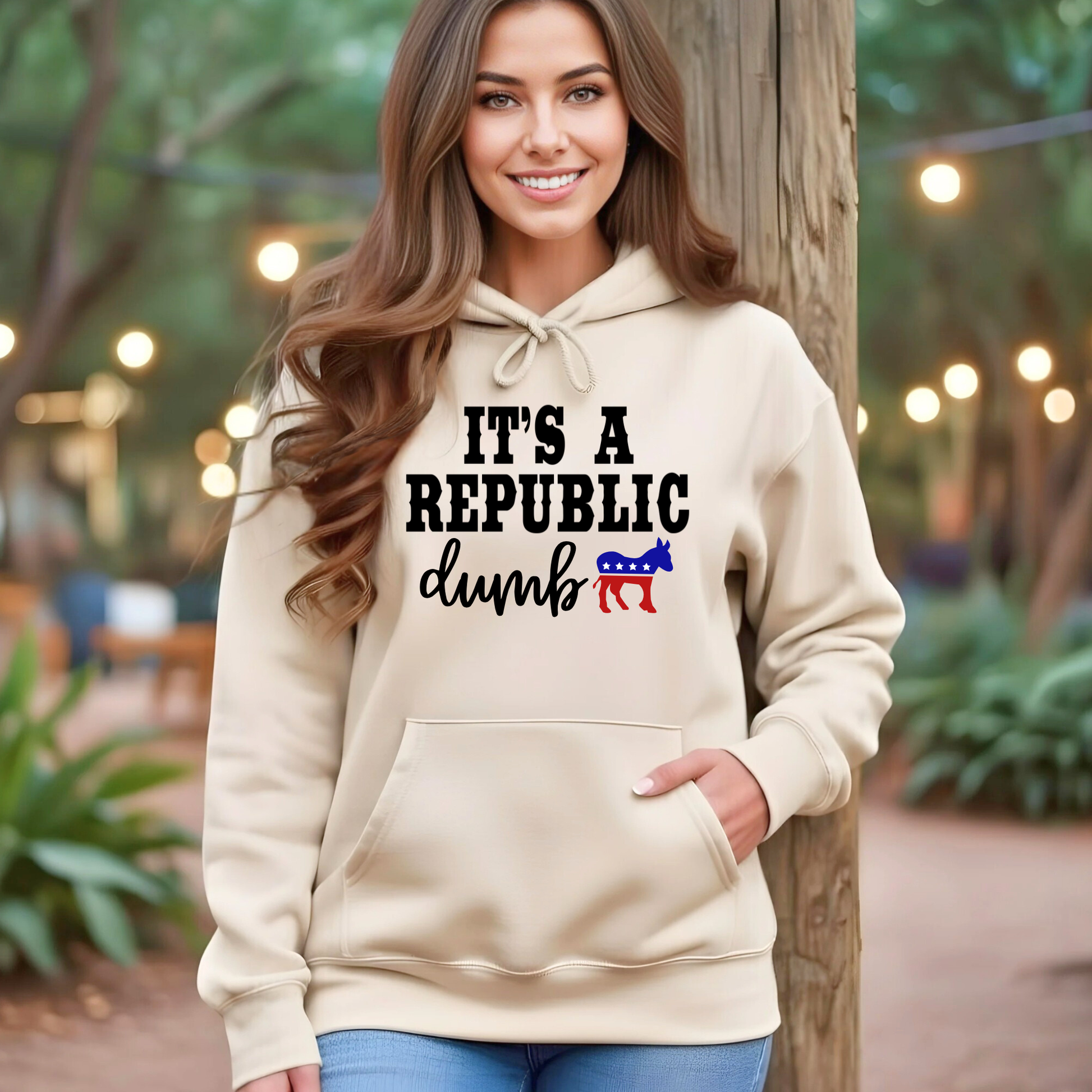 Woman wearing sand color pullover hoodie with “It’s a Republic Dumb” design outdoors