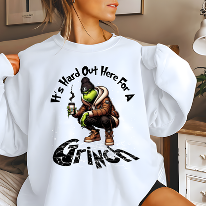 White unisex sweatshirt with It’s Hard Out Here for a Grinch graphic, winter street-style holiday design.