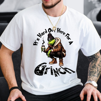 White unisex t-shirt featuring Hard Out Here for a Grinch graphic, casual indoor photo.