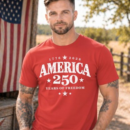Man wearing a red t-shirt with 'America 250 Years of Freedom' text, standing outdoors with an American flag in the background.