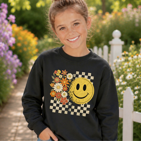 Young girl wearing a black sweatshirt with a smiley face design in a garden setting