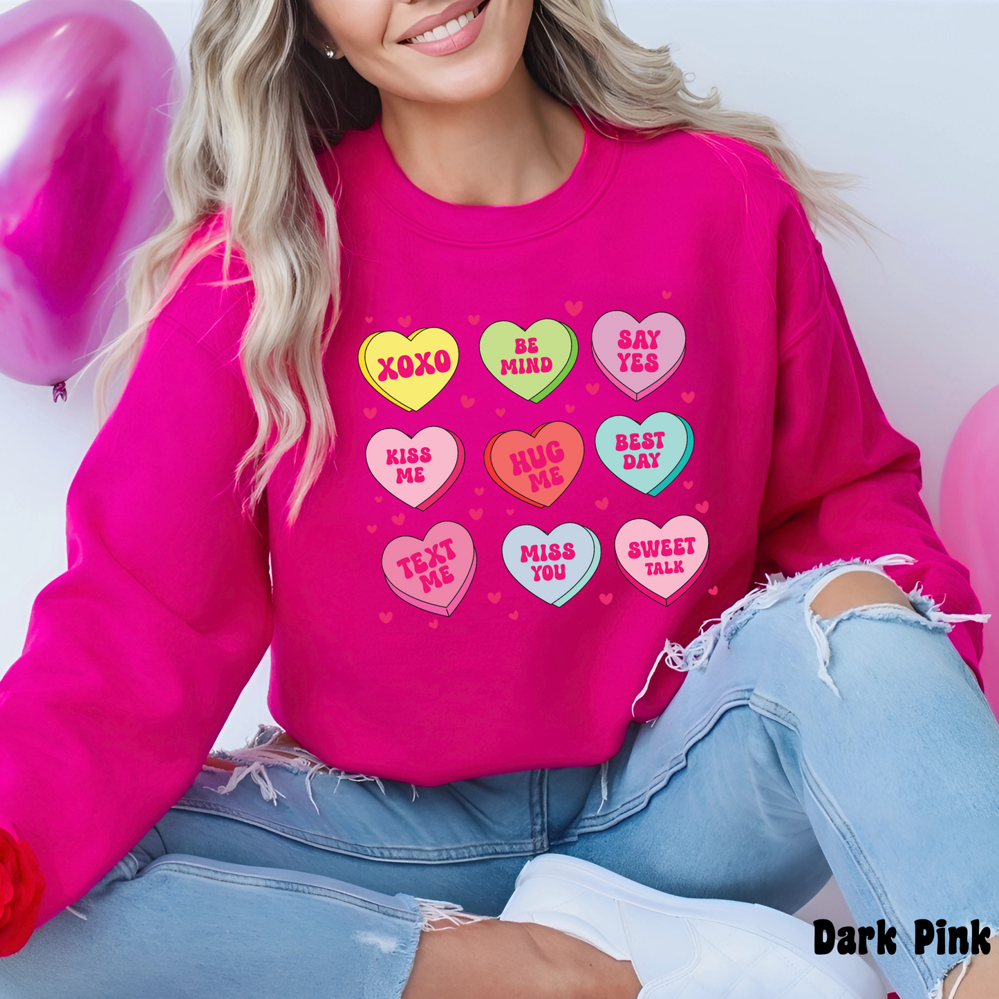 Woman wearing a dark pink Valentine’s sweatshirt featuring colorful candy conversation hearts with messages like “XOXO,” “Be Mine,” “Say Yes,” “Kiss Me,” “Hug Me,” and more.