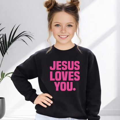Young girl wearing a black sweatshirt with 'Jesus Loves You' in pink text, standing indoors.