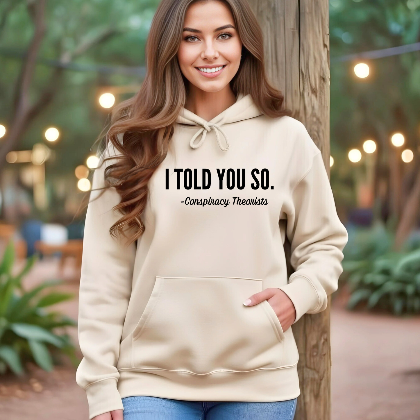 Woman wearing a Sand Colored hoodie with text 'I Told You So. - Conspiracy Theorists' outdoors.