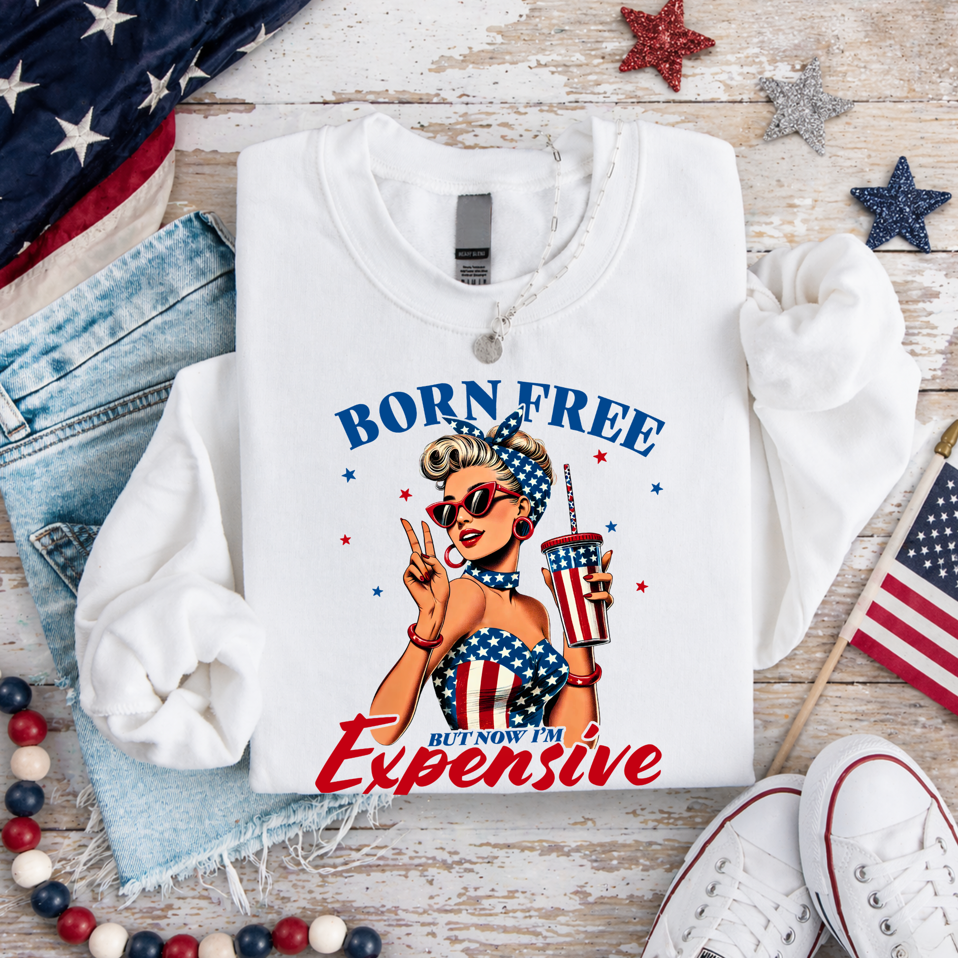 White sweatshirt with graphic design and text on a wooden surface with American flags and denim jeans.