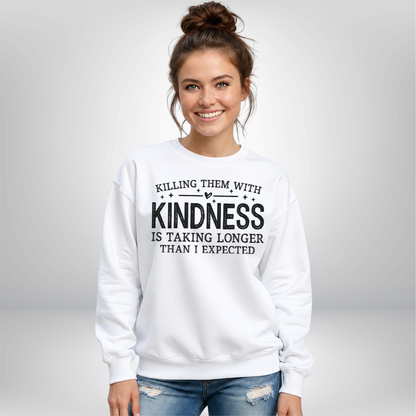 Woman against a gray background wearing a white Killing Them With Kindness crewneck sweatshirt with black lettering.