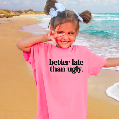 Child on a beach wearing a pink shirt with text, making a peace sign.
