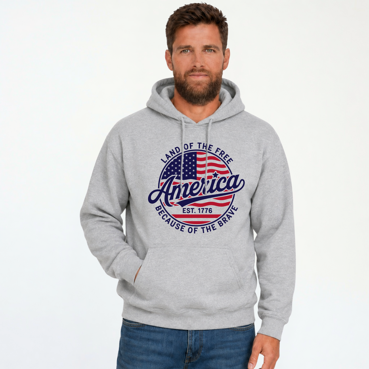 Male model wearing a sports gray pullover hoodie with a red, white, and blue circular America graphic reading Land of the Free, Est. 1776, and Because of the Brave.