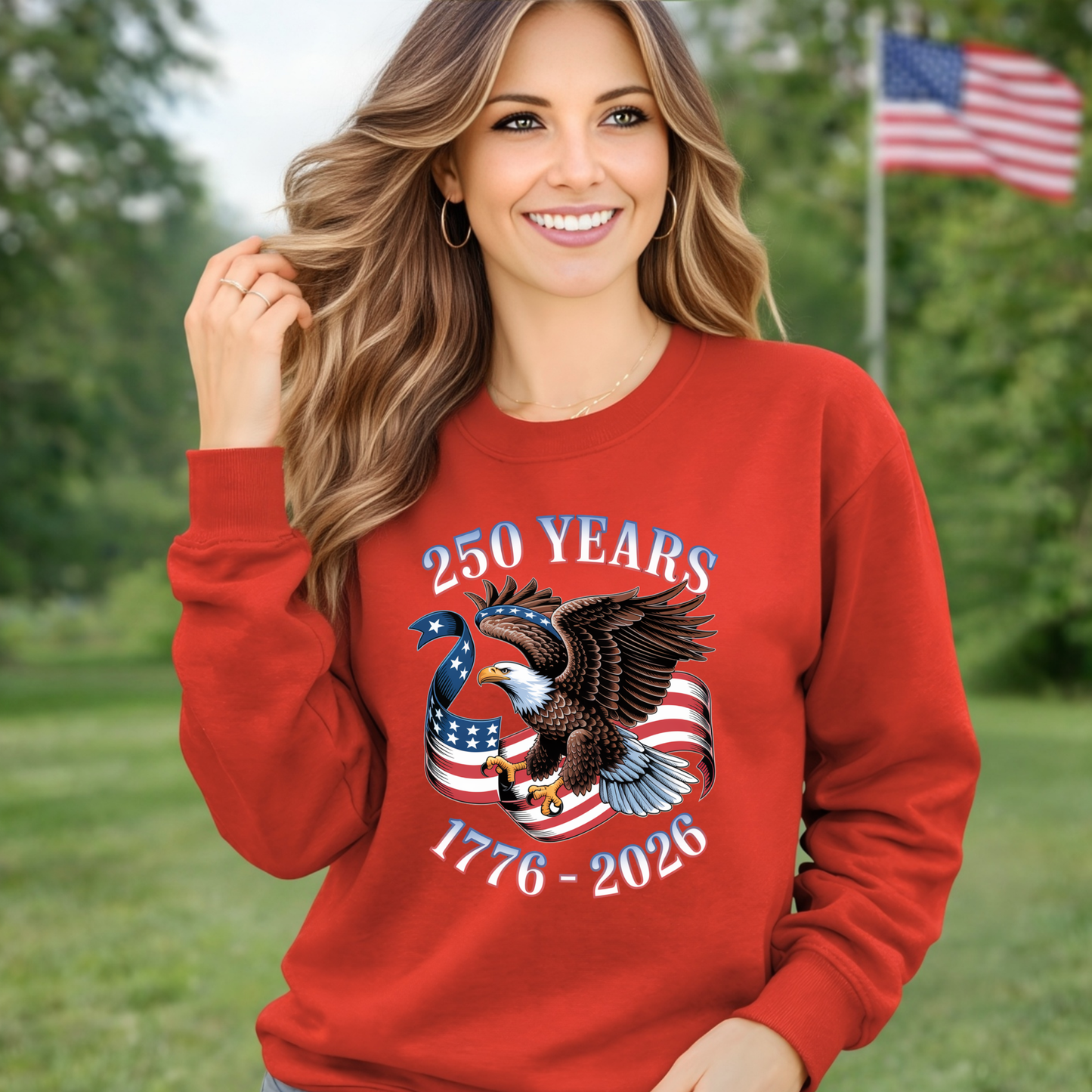 Woman wearing a red sweatshirt with an eagle and American flag design, standing outdoors with trees and an American flag in the background.