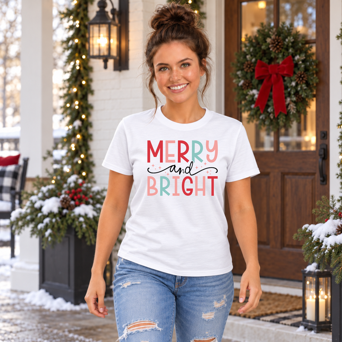 Woman wearing a white T-shirt with colorful Merry and Bright Christmas design on a snowy decorated porch