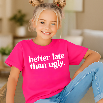 Young girl wearing a pink t-shirt with 'better late than ugly' text, sitting in a home setting.