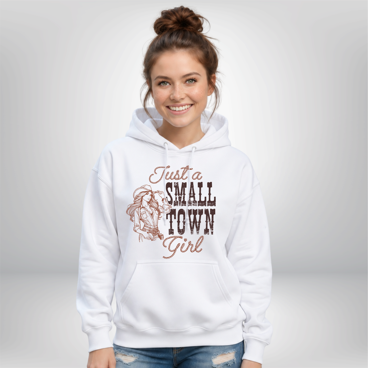Woman wearing a white hoodie with the “Just a Small Town Girl” western cowgirl graphic, shown against a clean light studio background.