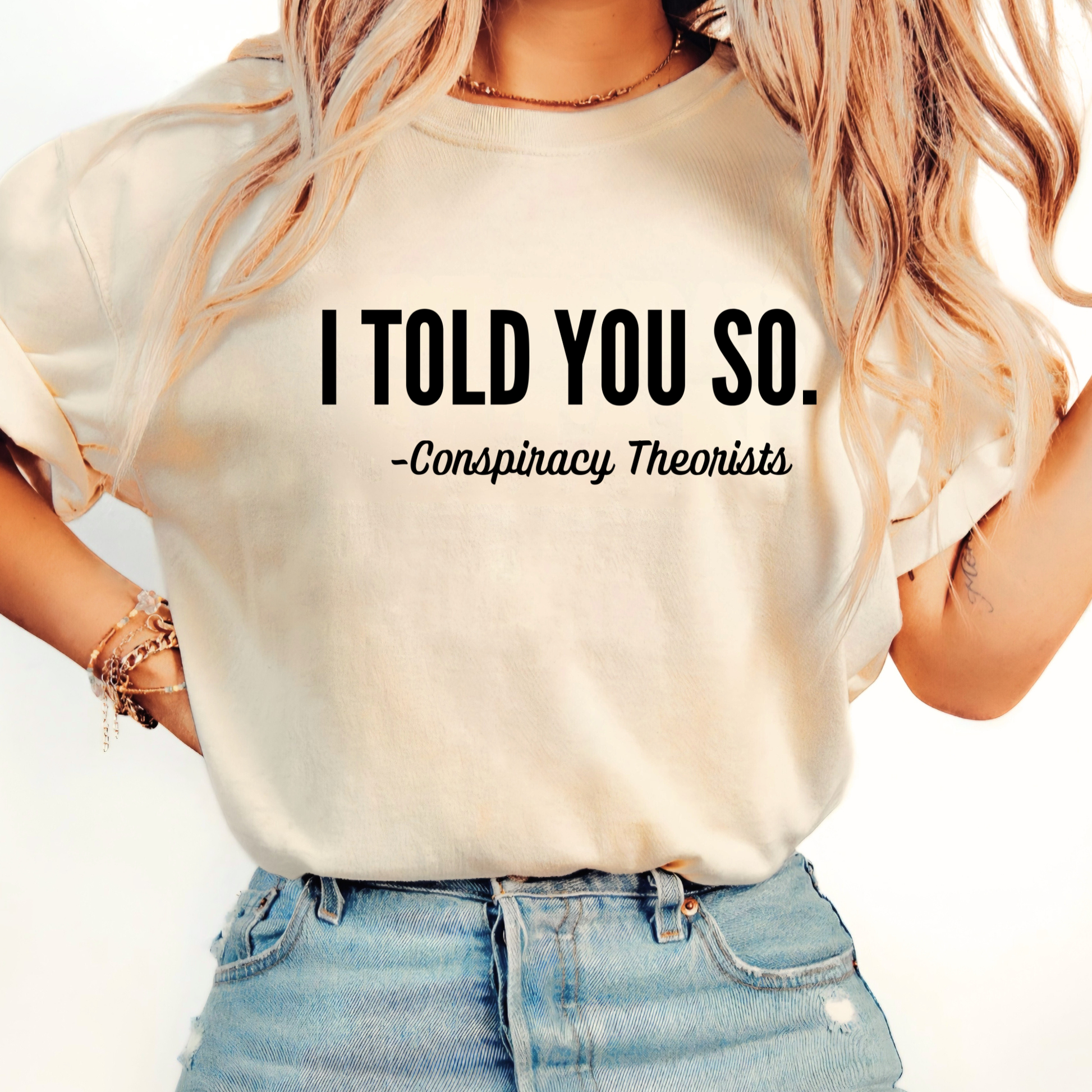 Person wearing a beige t-shirt with text 'I TOLD YOU SO. -Conspiracy Theorists' on a plain background