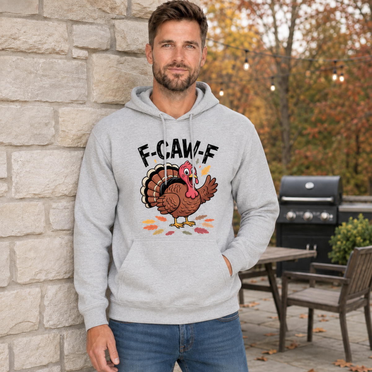 Man wearing a sports gray hoodie with a colorful F-CAW-F turkey graphic in a fall patio setting.