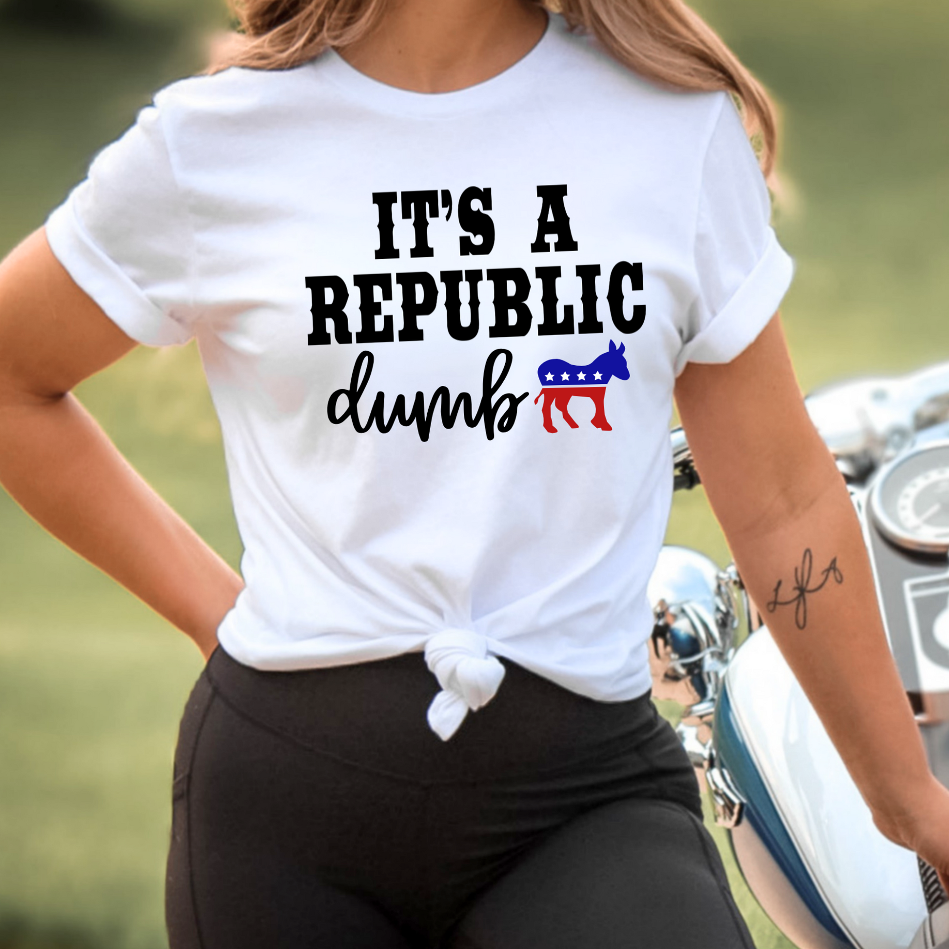 Person wearing a white t-shirt with political text and symbols, standing next to a motorcycle.