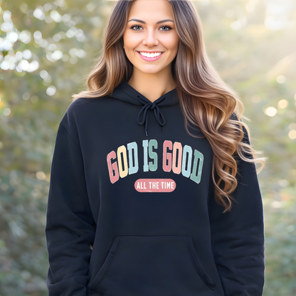 Woman wearing a black hoodie with 'GOD IS GOOD ALL THE TIME' text, standing outdoors.