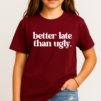 Person wearing a maroon t-shirt with 'better late than ugly' text on a plain background