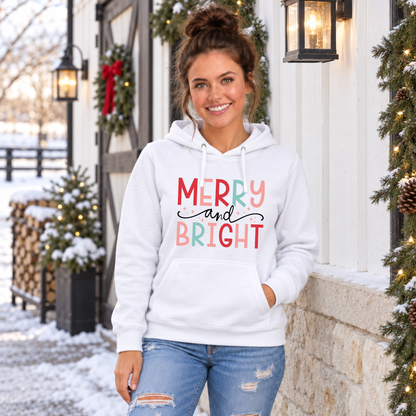 Woman wearing a white hoodie with colorful Merry and Bright Christmas design outside a snowy holiday home