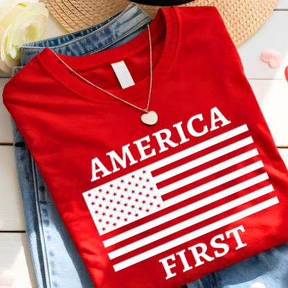 Red t-shirt with 'AMERICA FIRST' text and American flag design on a wooden surface.