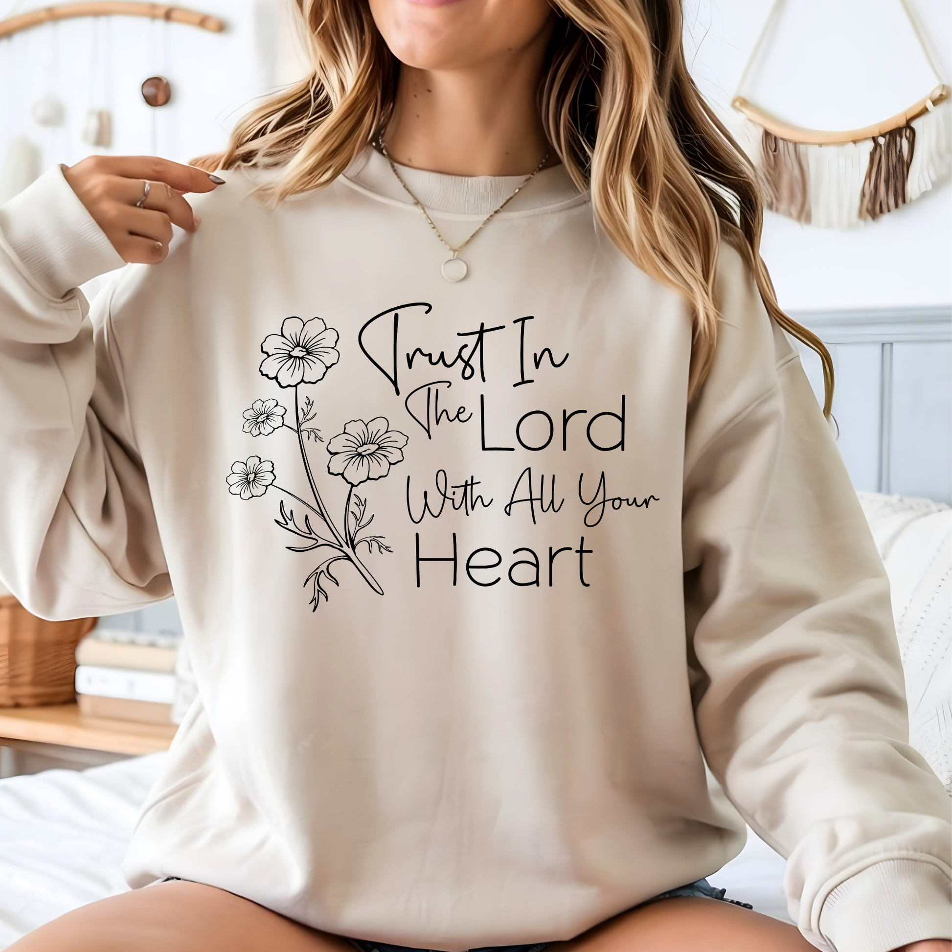 Person wearing a beige sweatshirt with 'Trust In The Lord With All Your Heart' text and floral designs.