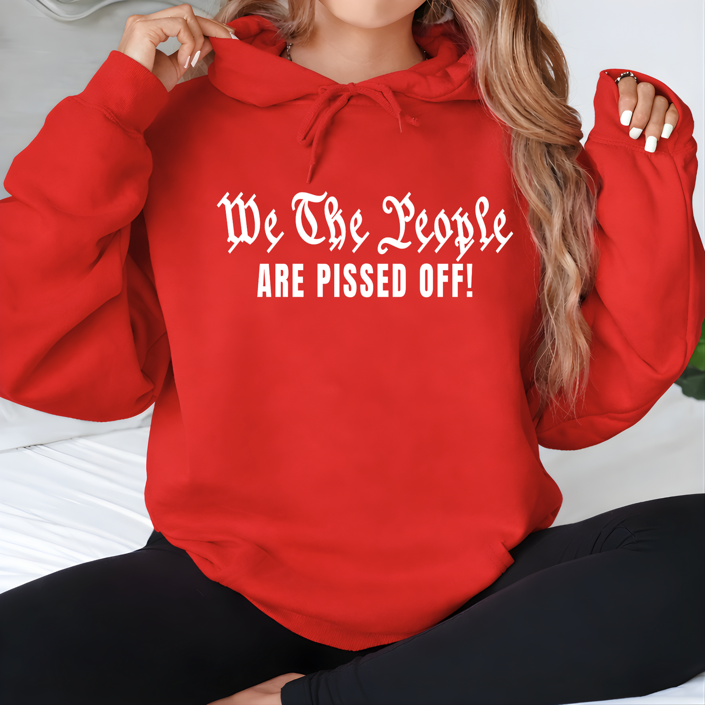 Person wearing a red hoodie with text 'We The People ARE PISSED OFF!' sitting on a white surface.