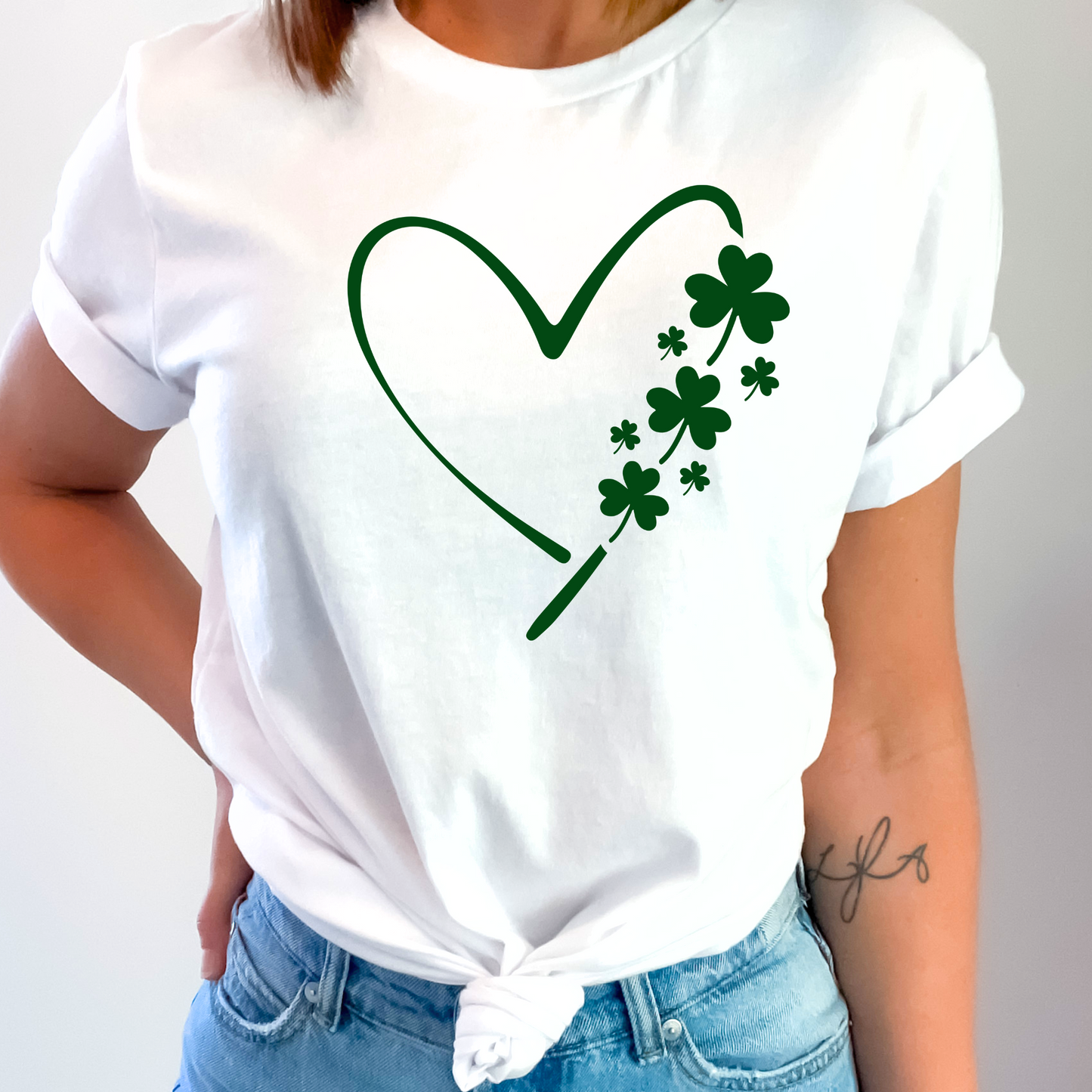A woman wearing a white T-shirt with a minimalist green heart and shamrock design, perfect for St. Patrick’s Day celebrations.