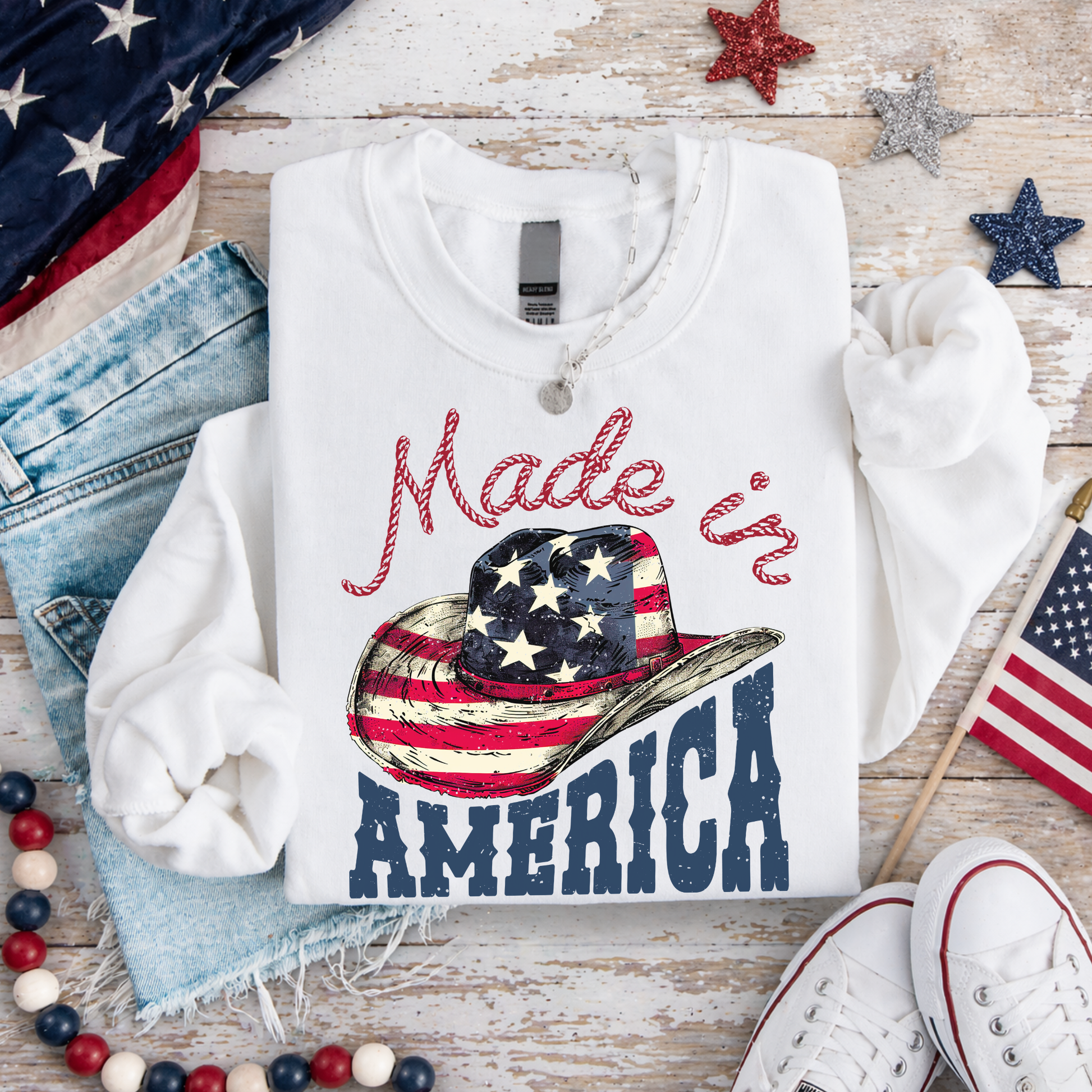 White sweatshirt with 'Made in America' graphic on a wooden surface with American flags and denim.